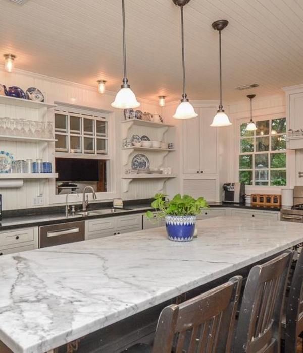 Bright white kitchen with marble island, pendant lights, open shelves, and a potted plant centerpiece.