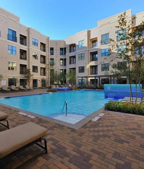 Modern apartment courtyard with blue swimming pool, brick patio, lounge chairs, and multi-story buildings