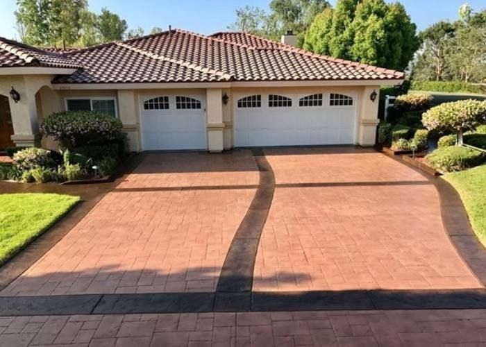 Large brick driveway leading to a suburban house with a three-car garage and tiled roof