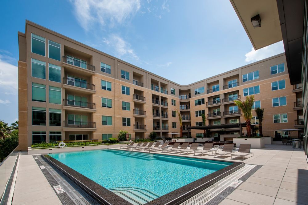 Modern apartment courtyard with a swimming pool and surrounding balconies under a blue sky