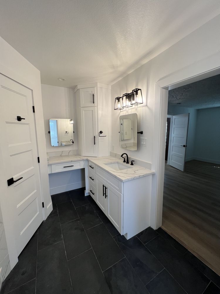 Modern white bathroom with black tile floor, vanity, mirror, and wall sconce lighting