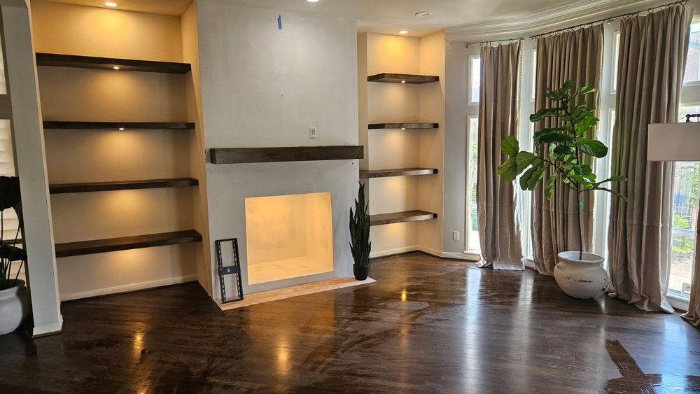 Living room with built-in shelves, fireplace, dark wood floors, and tall curtains beside a potted plant.