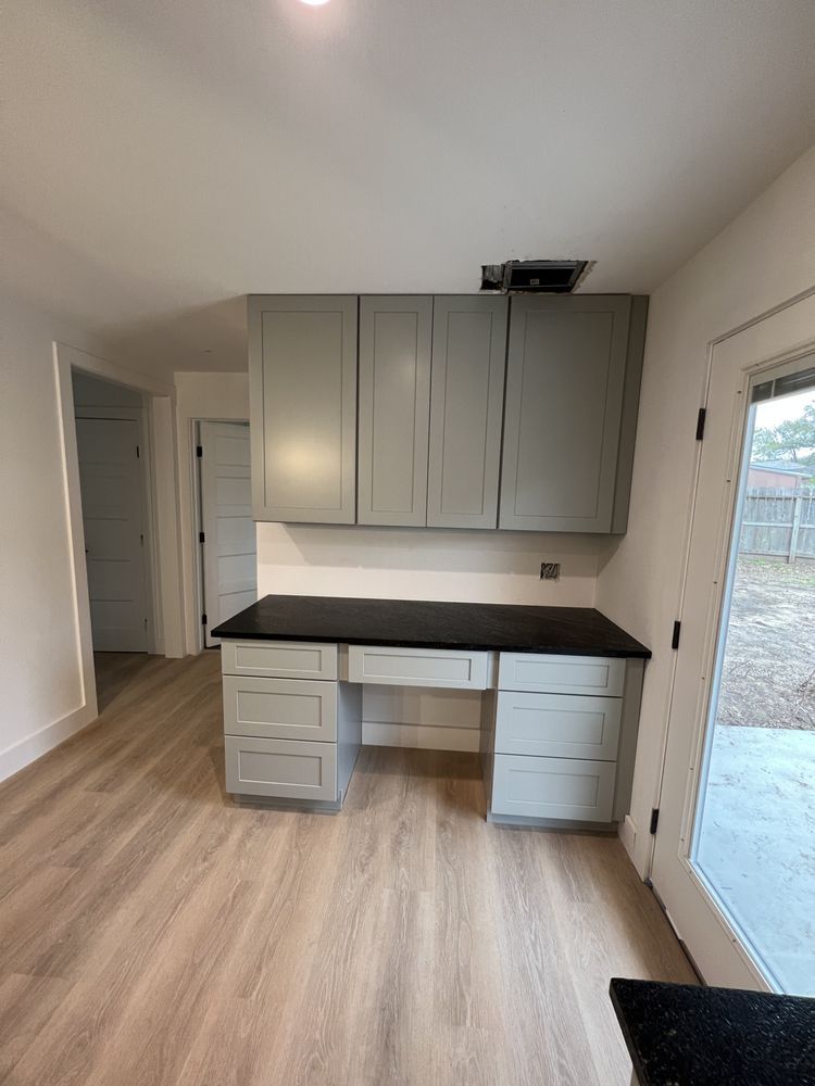 Small room with built-in gray cabinets, black countertop, and wood-look flooring near a glass door.