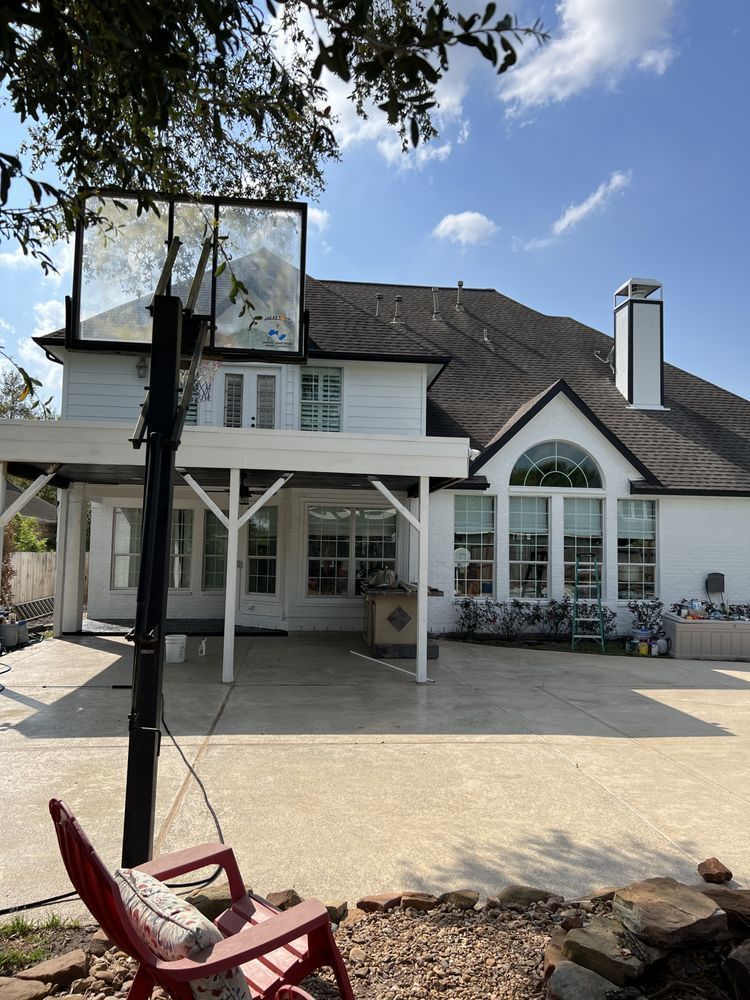 Backyard view of a white house with patio, basketball hoop, and red chair on a paved driveway.