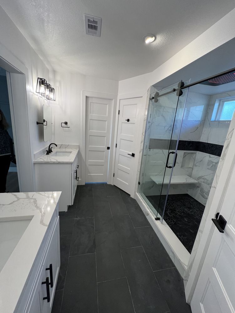 Modern white bathroom with dark tile floor, vanity, toilet room, and glass-enclosed shower.