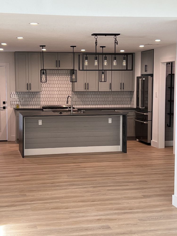 Modern kitchen with gray island, pendant lights, stainless appliances, and wood flooring