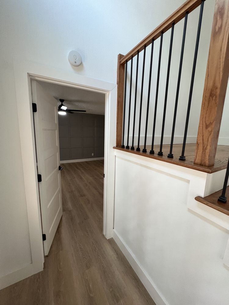 Hallway with wood flooring, white walls, and a staircase railing on the right leading to a room ahead.