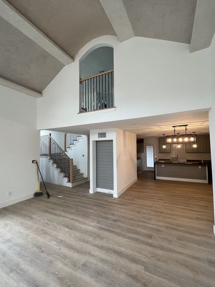 Spacious open-plan living room with high vaulted ceiling, staircase, and kitchen area in a modern home