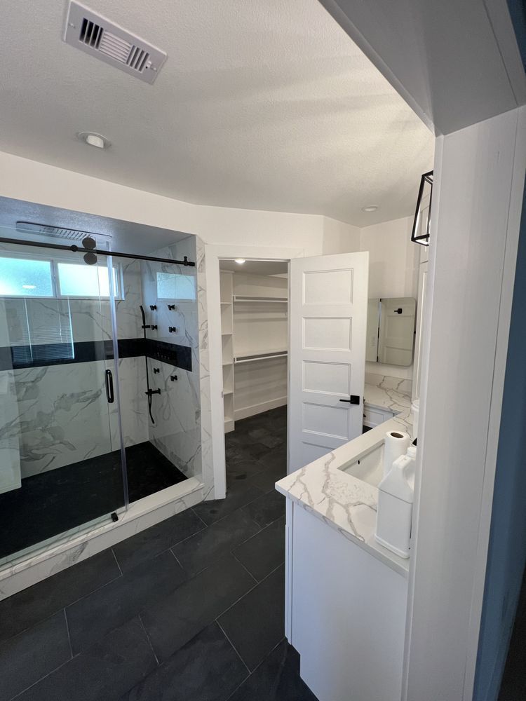 Modern bathroom with glass shower, white vanity, open shelving, and dark tile floor