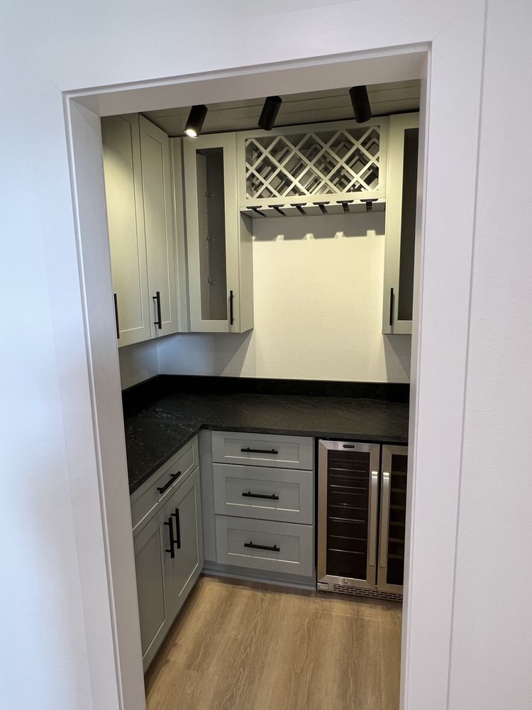 Built-in corner bar nook with gray cabinets, black countertop, wine rack, and wood floor