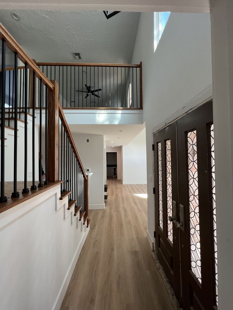 Bright foyer with staircase, wood floors, balcony railing, and front double doors with glass panels.