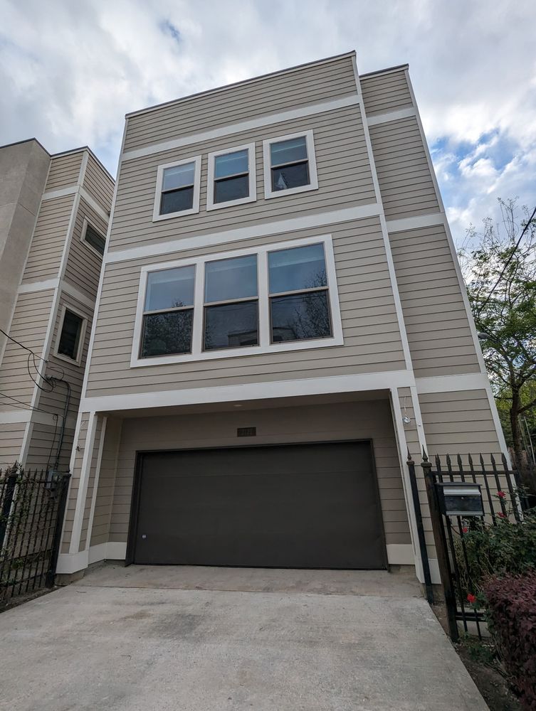 Three-story beige townhouse with a two-car garage and large windows under a cloudy sky