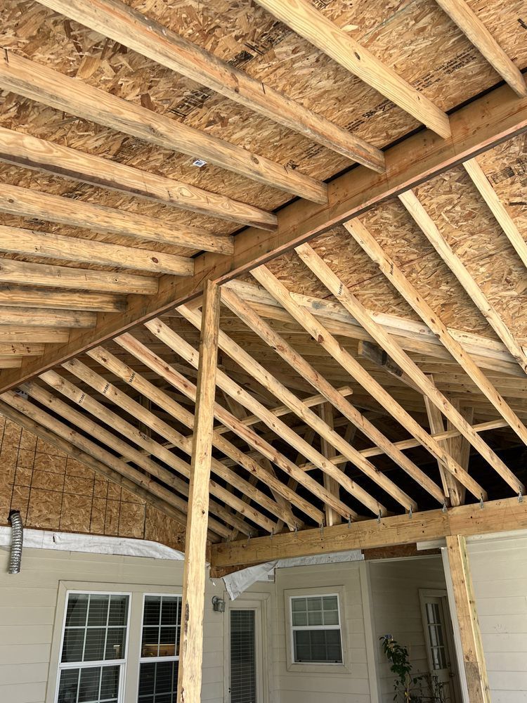 Exposed wooden roof framing under construction above a patio and house exterior
