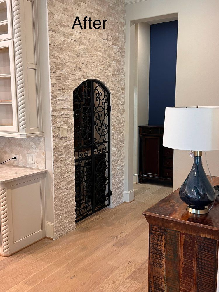 Stone fireplace wall with black arched screen in a bright room, hardwood floor, and lamp on a wooden cabinet