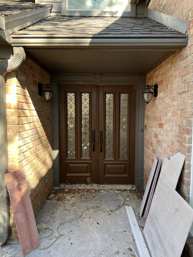 Brick entryway with dark double doors, sidelights, and construction debris on the ground
