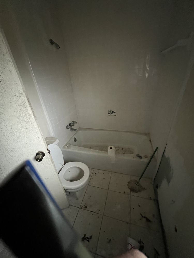 Small, dirty bathroom with a toilet, bathtub, tiled floor, and scattered debris