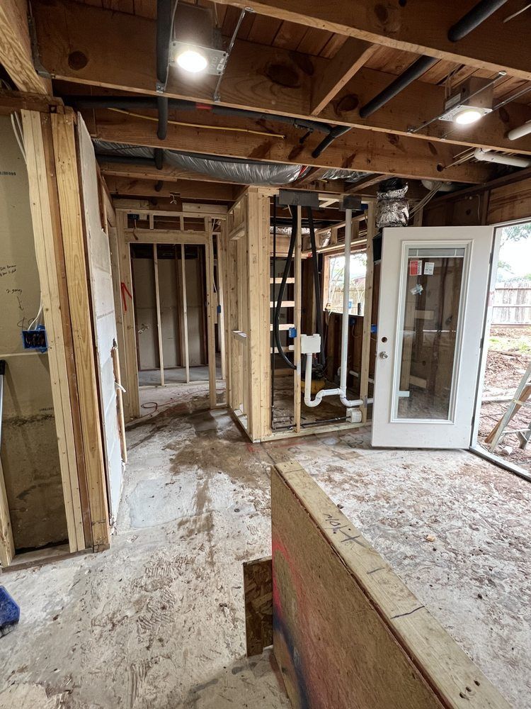 Interior under renovation with exposed studs, wiring, debris, and an open door to the outside.