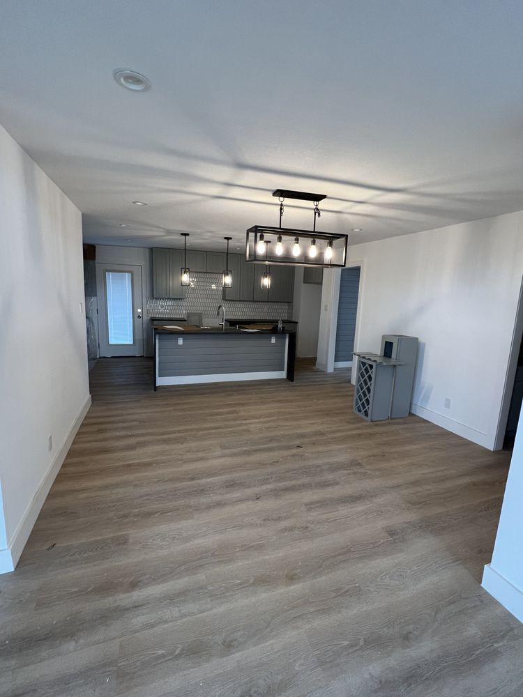 Empty open-plan living room with wood floors and kitchen island, modern pendant lights, and white walls