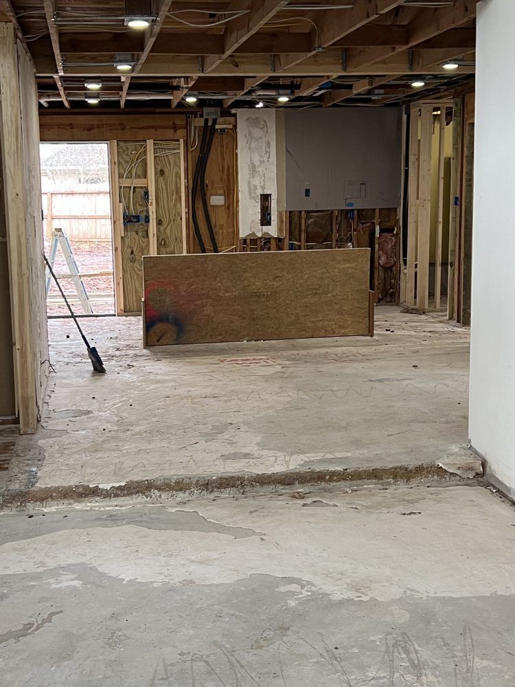 Partially demolished interior with exposed studs, concrete floor, and a leaning plywood barrier.
