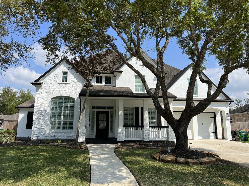 White suburban house with black trim, large front windows, and a tree-lined front yard.