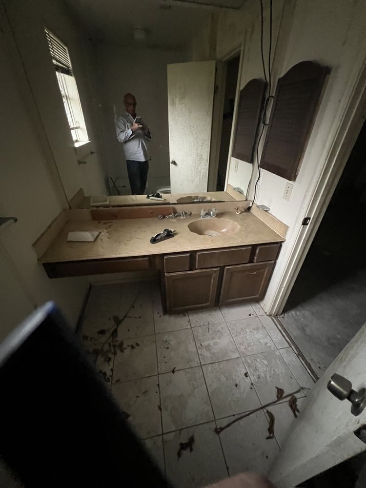 Damaged bathroom with broken mirror, overturned sink cabinet, and debris on tiled floor.