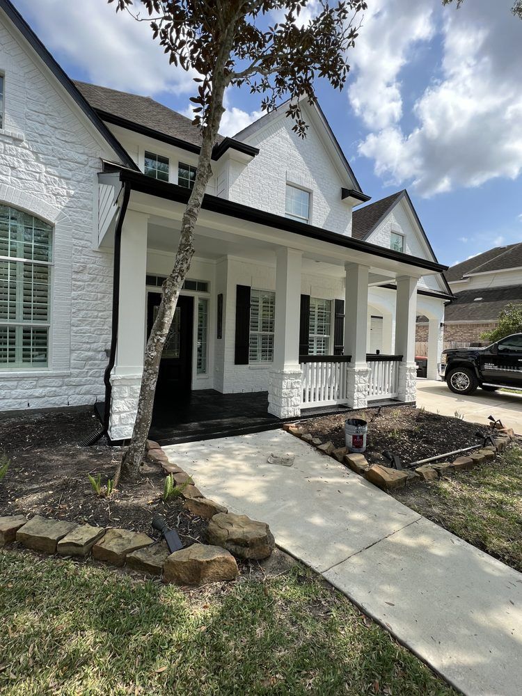 White brick house with black porch, concrete walkway, and young tree in the front yard