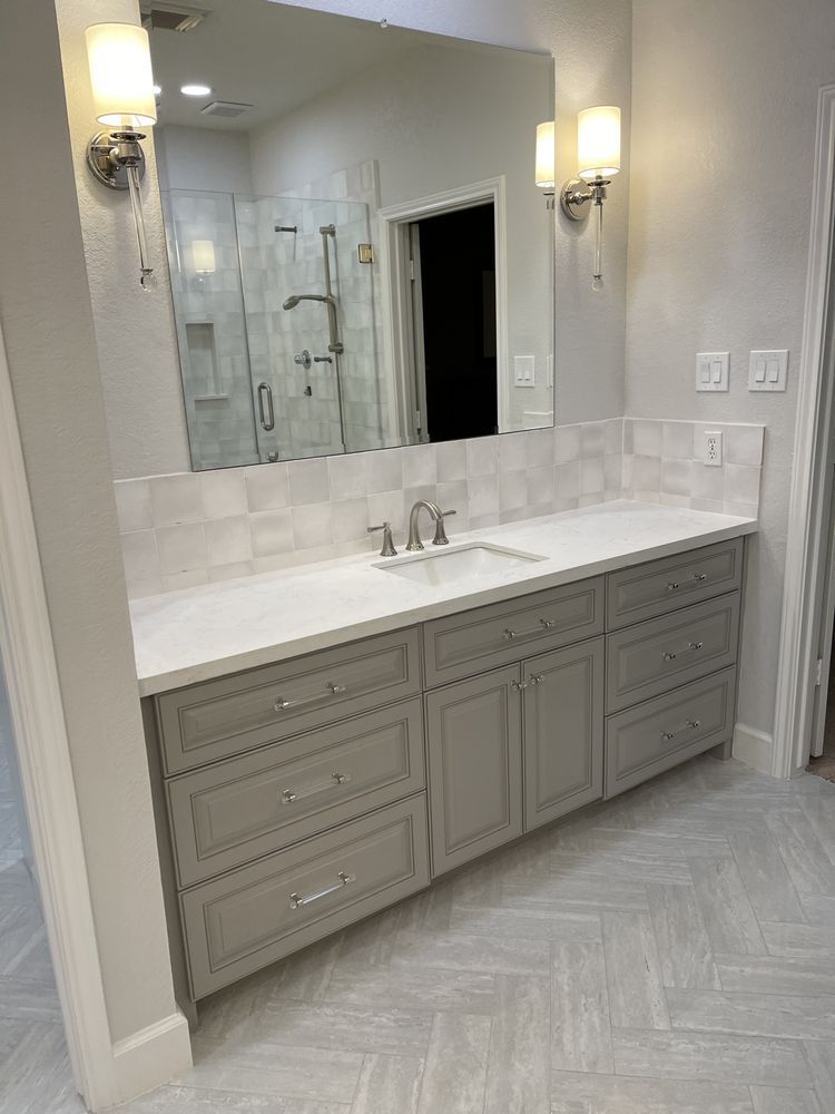 Modern bathroom vanity with gray cabinets, white countertop, large mirror, and wall sconces
