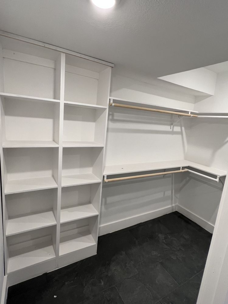Empty white walk-in closet with shelves, hanging rods, and black carpet flooring.