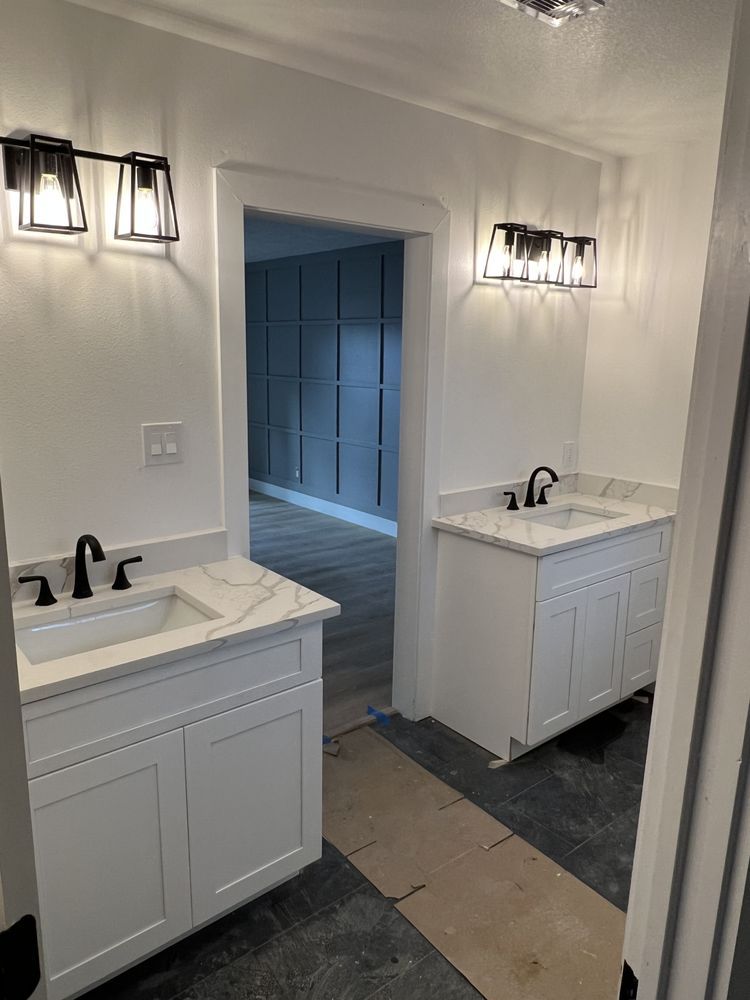 Bright bathroom with two white vanities, wall sconces, and an open doorway to a tiled shower area.