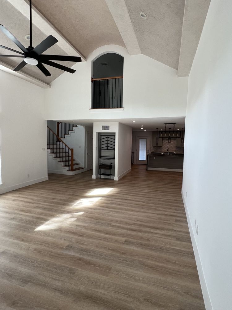 Spacious empty living room with vaulted ceiling, ceiling fan, staircase, and wood-look flooring
