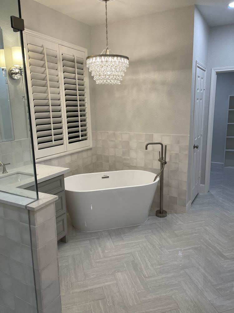 Modern bathroom with freestanding tub, glass shower, crystal chandelier, and herringbone tile floor