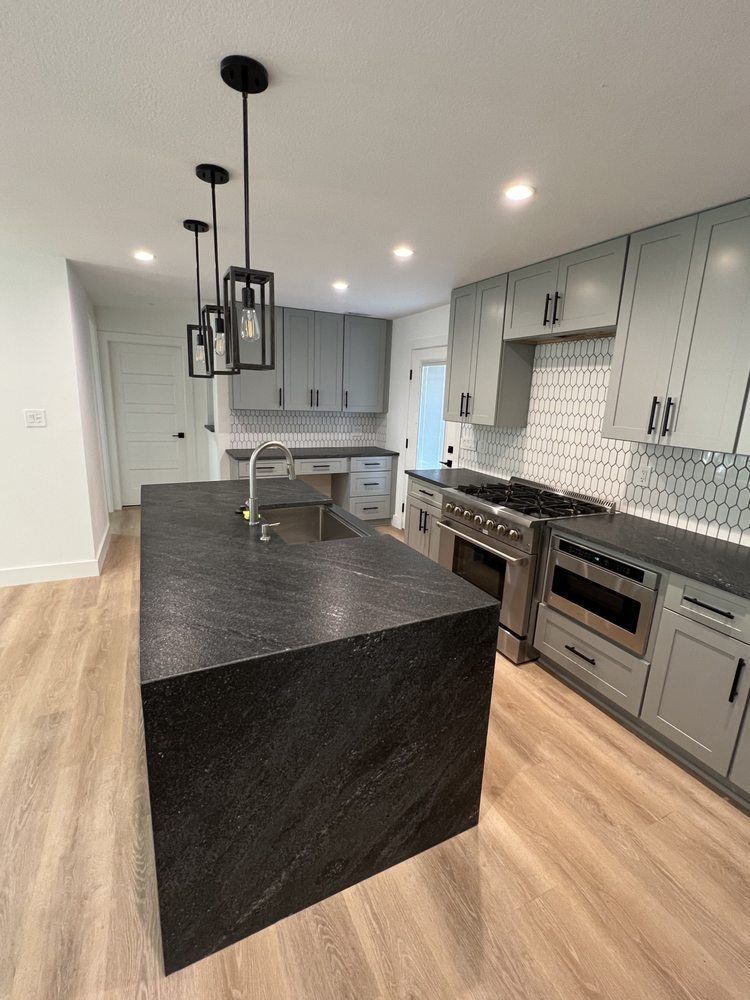 Modern kitchen with gray cabinets, black island, pendant lights, and stainless steel appliances