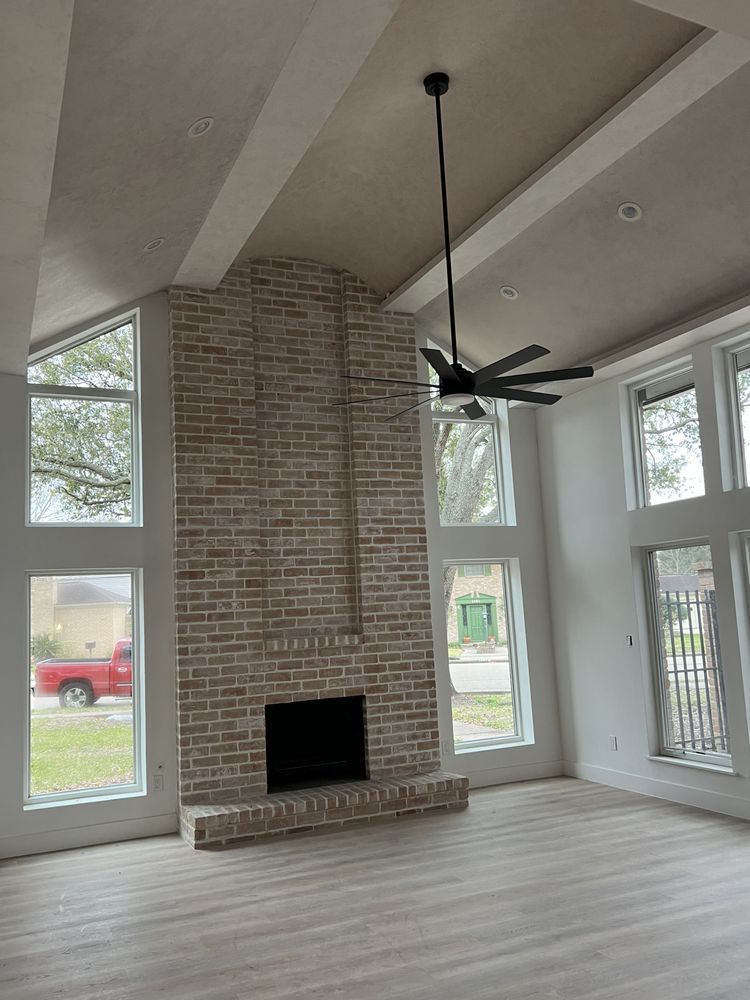 Modern living room with vaulted ceiling, brick fireplace, large windows, and a black ceiling fan