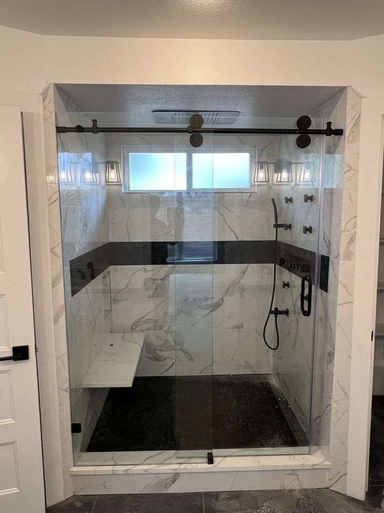 Glass walk-in shower with black trim, white tile, and a built-in bench, viewed from the doorway