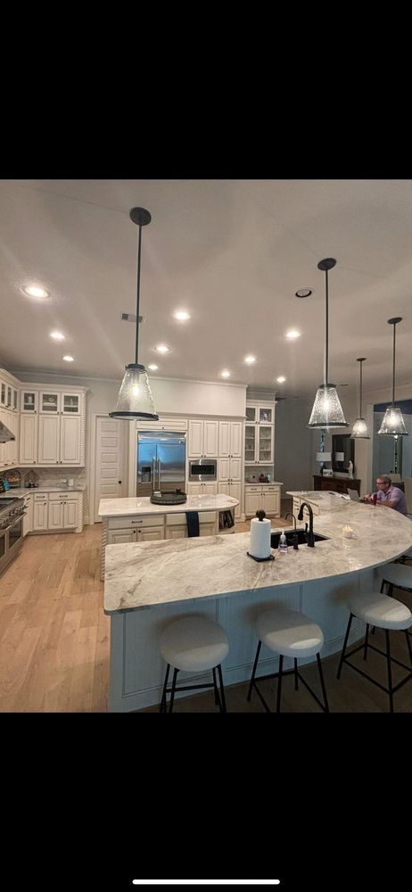 Modern white kitchen with marble island, pendant lights, bar stools, and hardwood floors