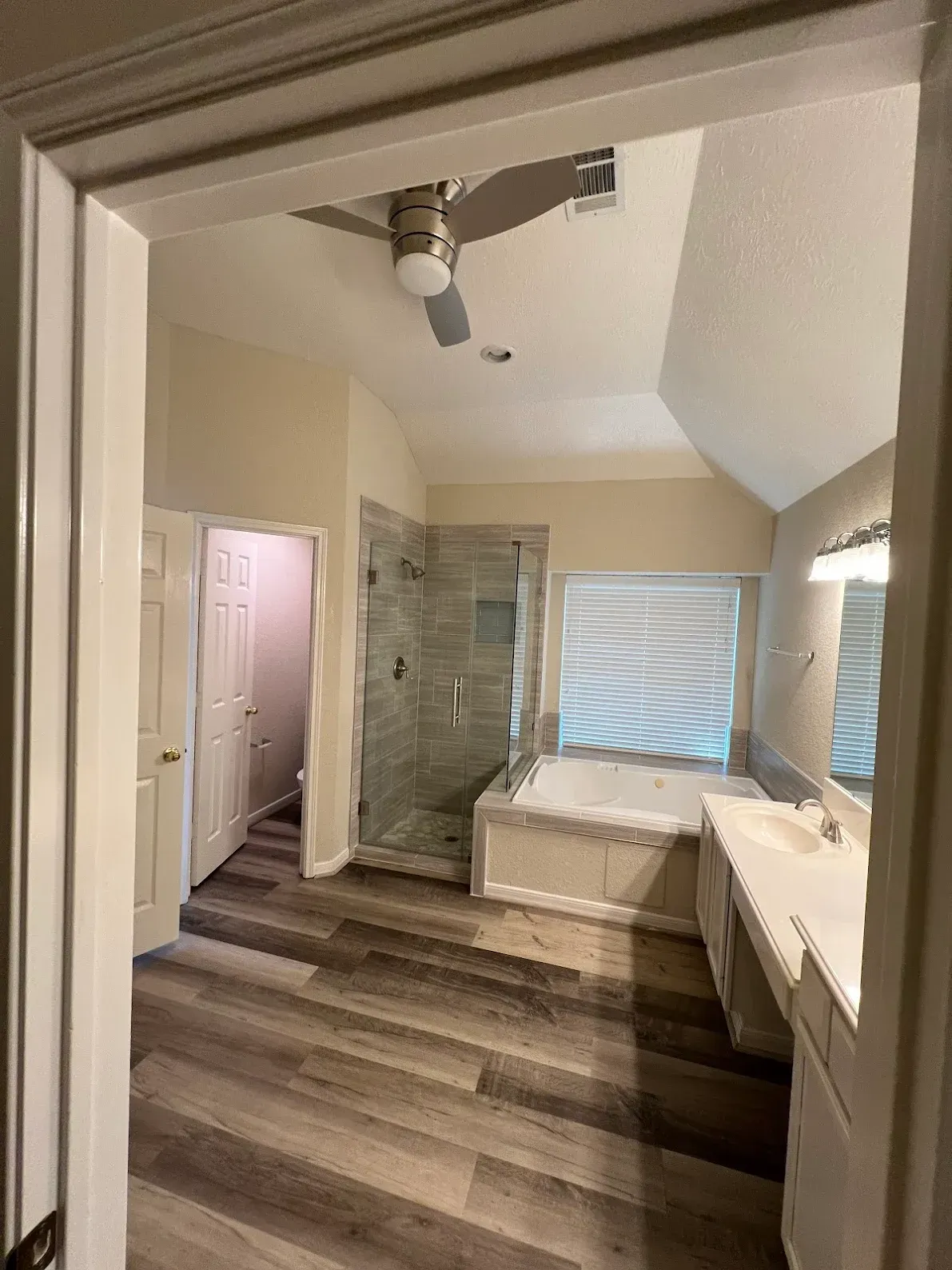 Bathroom with dark wood floor, glass shower, tub under window, and vanity on the right