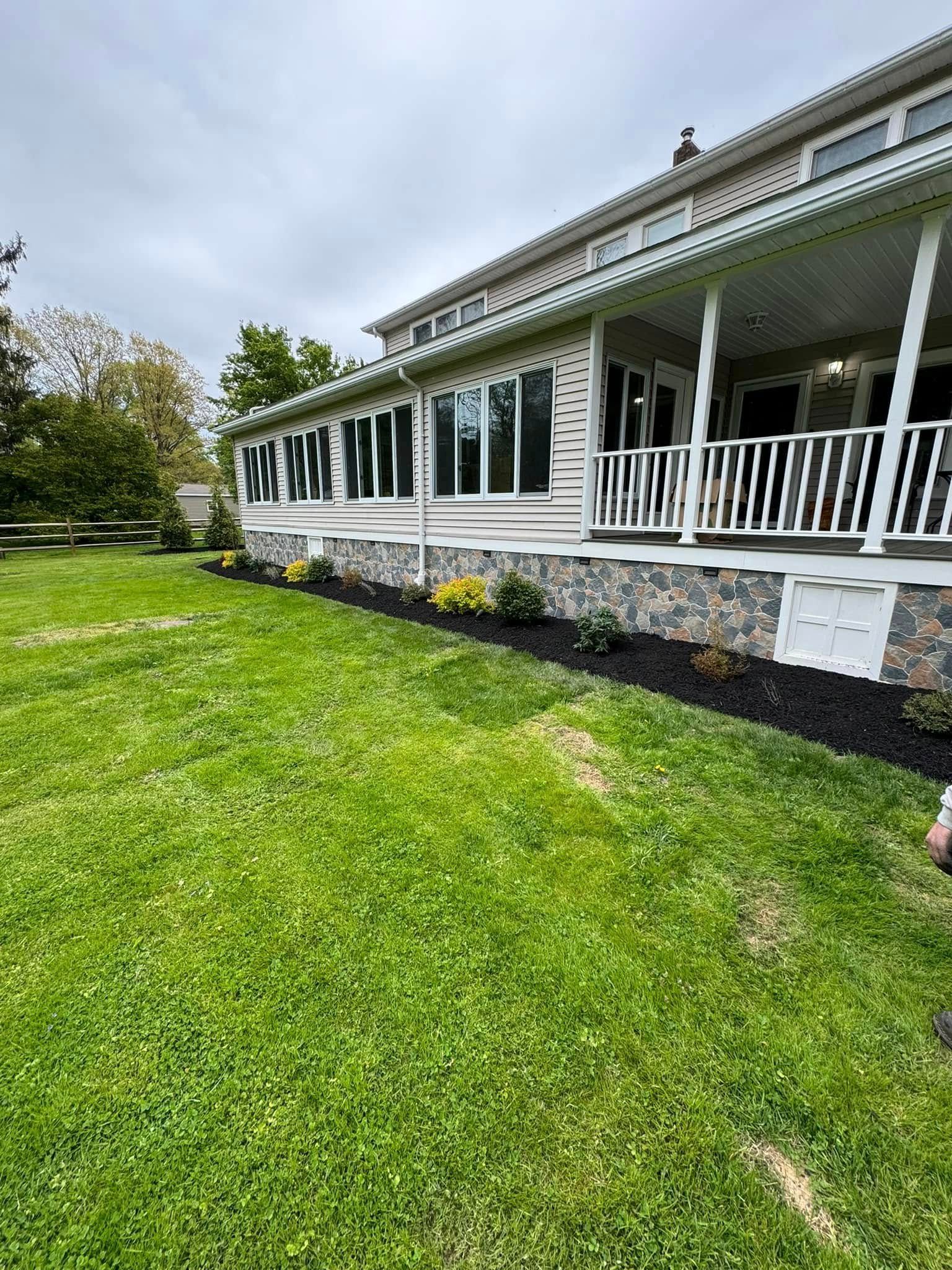 Lawn in front of a house with a stone and wood facade. Flower bed with mulch and shrubs along the foundation.