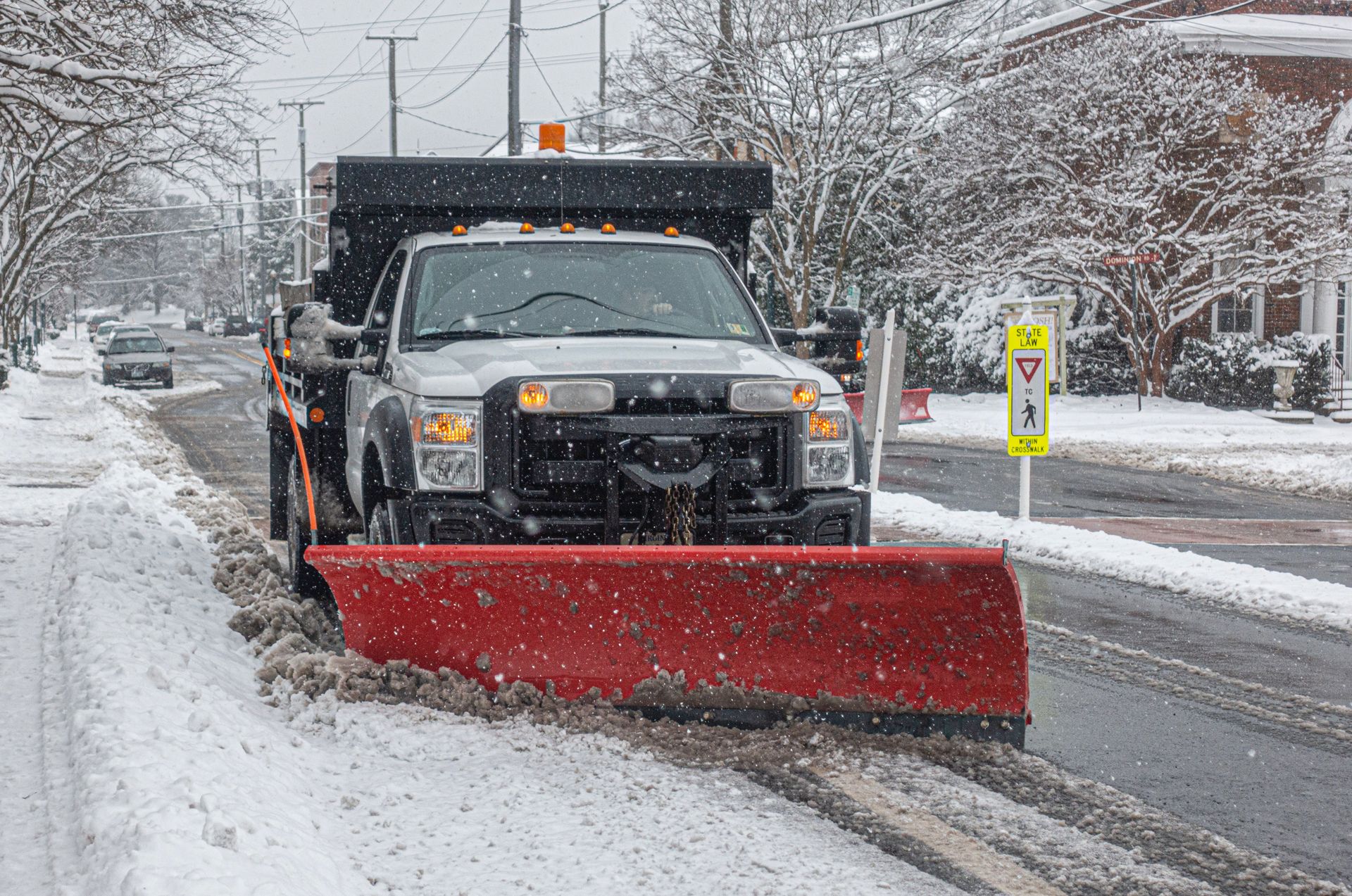 Snowplow clearing snow from a residential street during a snowfall.