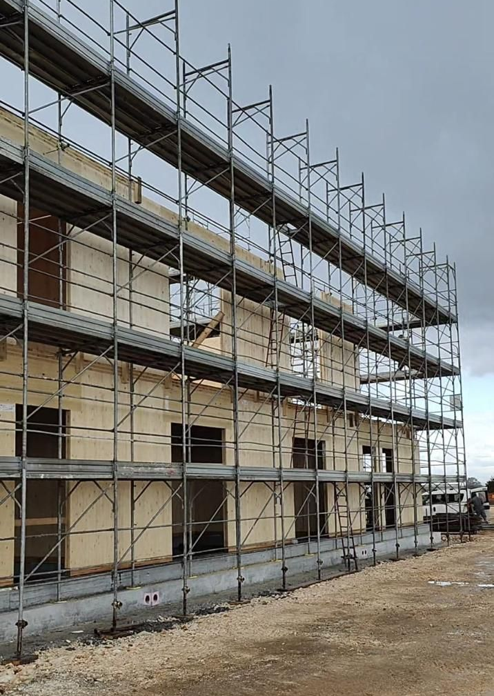 Un'imponente impalcatura metallica circonda la facciata color crema di un edificio in costruzione.
