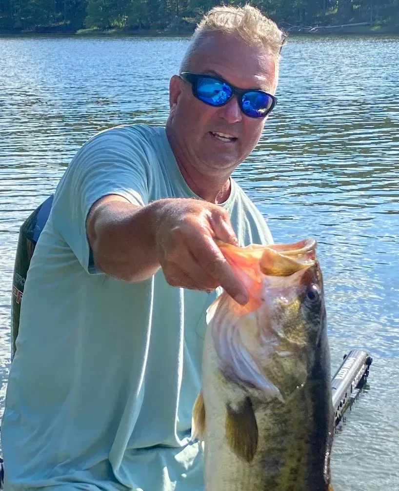 a man wearing sunglasses is holding a large fish in his hand .