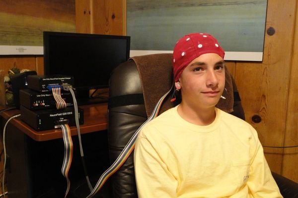 Person in a red bandana and yellow shirt sitting in an office chair in a wood-paneled room.