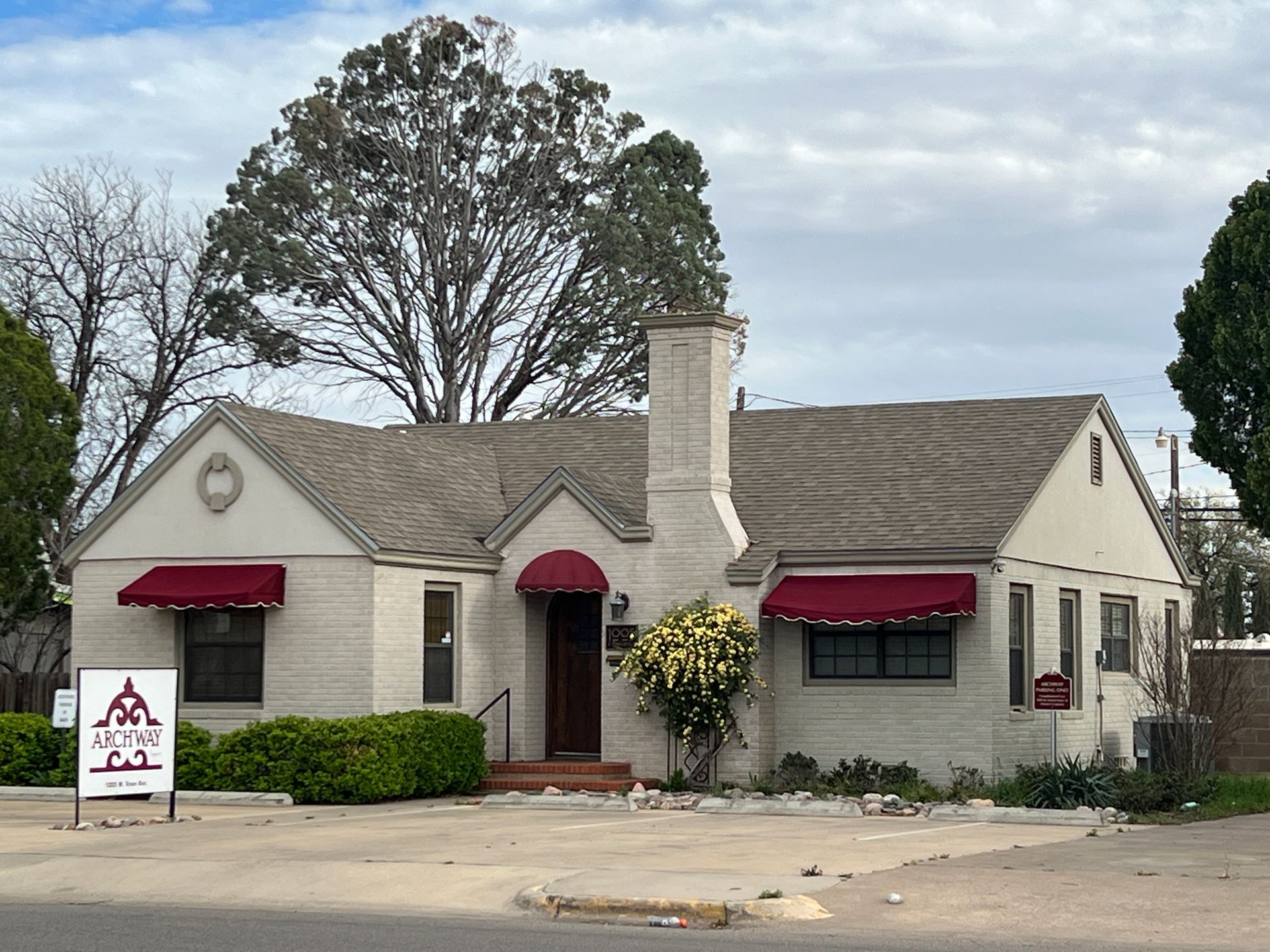Small white stucco building with red awnings and a sign in front on a cloudy day