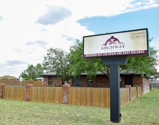 Sign for Archway building with wood fence and brick structure in a grassy lot