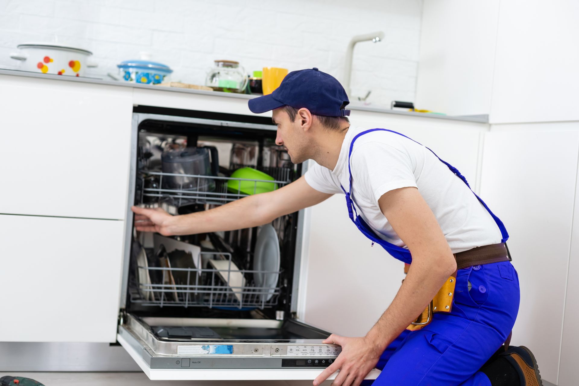 Technician in blue overalls loading a dishwasher in a bright kitchen