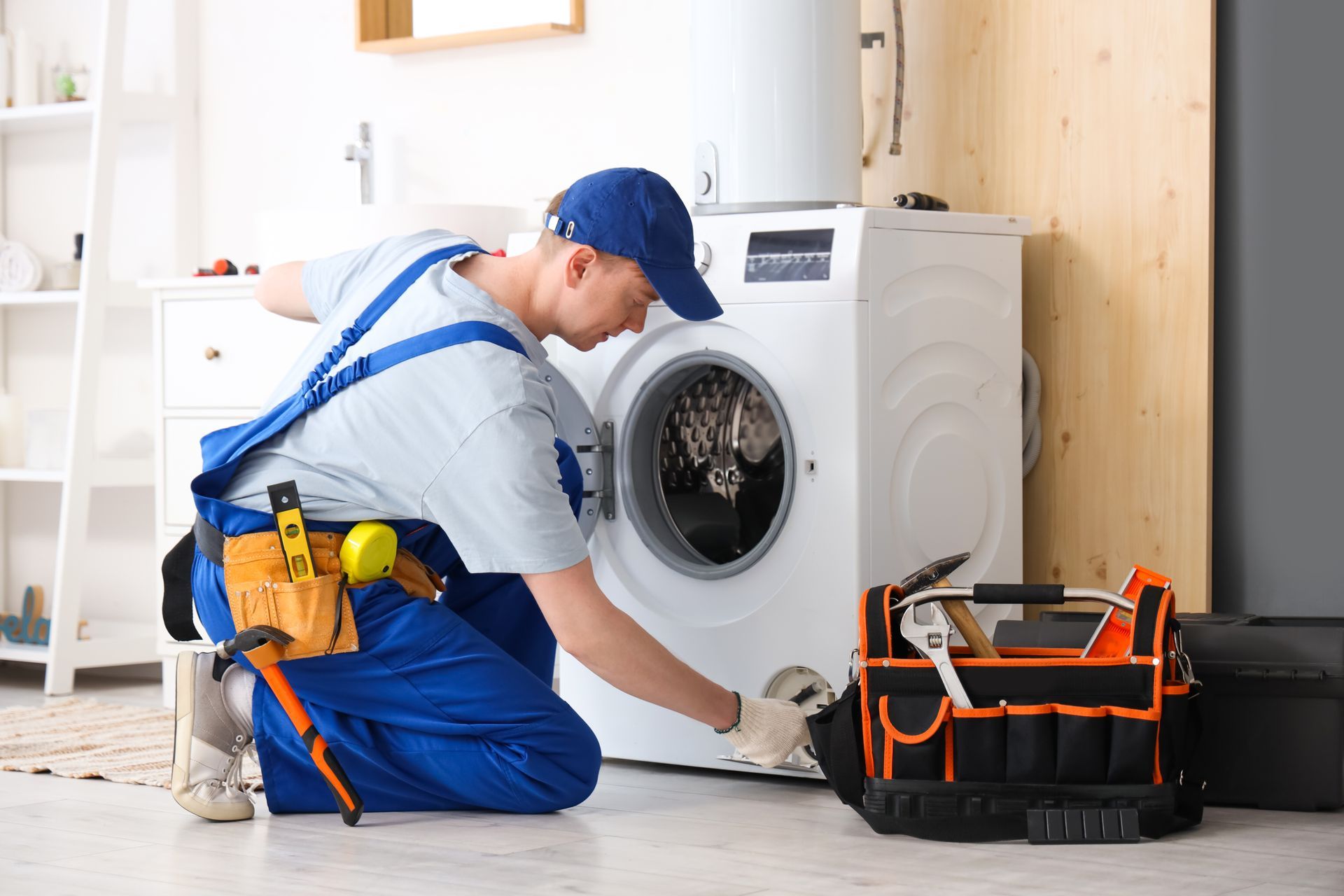 Technician in blue overalls repairing a front-loading washing machine in a laundry room Technician in blue overalls repairing a front-loading washing machine in a laundry room