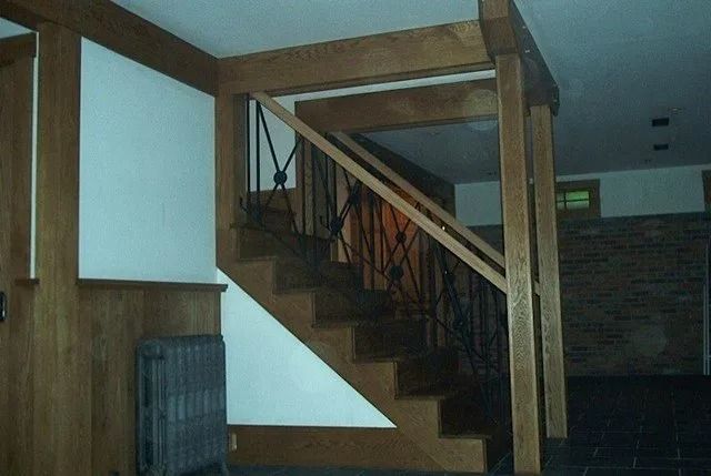 Wooden staircase in a dim interior hallway with railing and white walls