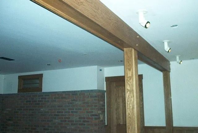Interior room with exposed wooden beams, brick half wall, and white ceiling lights.