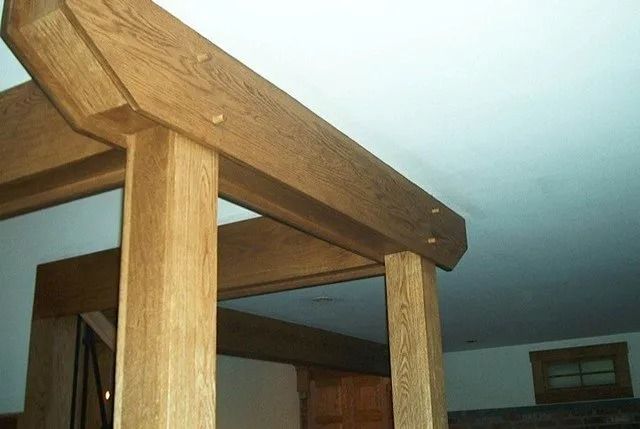 Close-up of a wooden bed frame with posts and a canopy beam in a bedroom