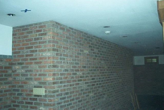 Brick interior hallway with white ceiling and recessed lights, leading to a dark doorway.