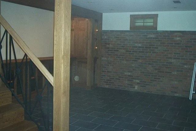 Empty brick-walled room with a staircase, wooden post, and dark tiled floor